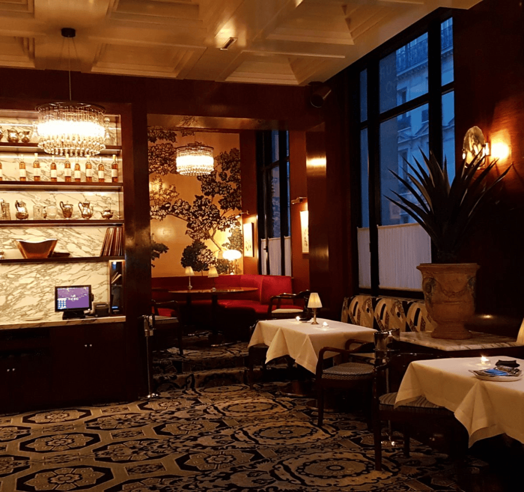 Cozy restaurant interior featuring elegant decor with patterned rugs, marble surfaces, and ambient lighting, including chandeliers and candles on tables.