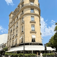 A street view of a stylish building featuring a restaurant named L'Avenue, with outdoor seating and a clear blue sky in the background.