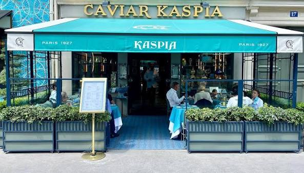 Exterior view of Caviar Kaspia restaurant in Paris, featuring green awning and outdoor seating with patrons dining.